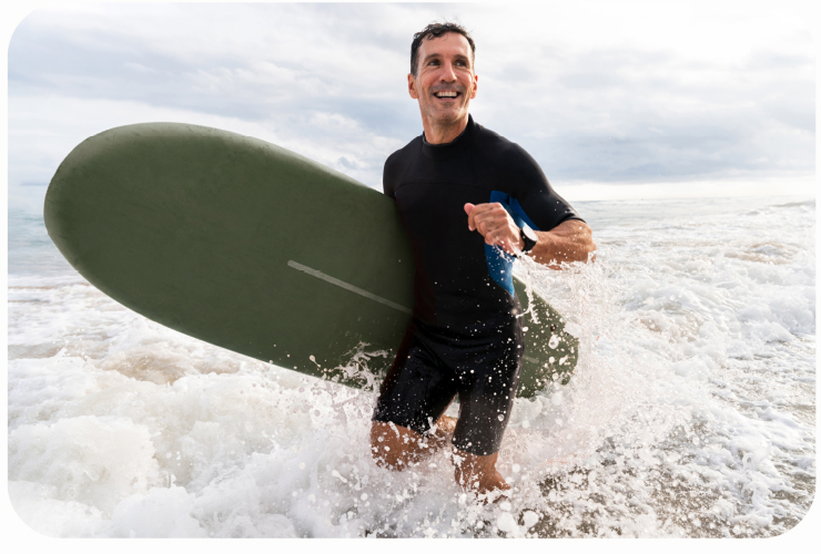 A smiling man carrying a surfboard through ocean surf